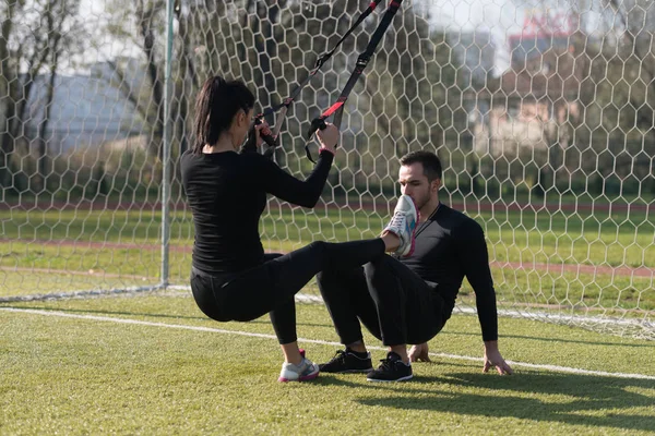 Casal jovem exercitando correias Trx no parque — Fotografia de Stock