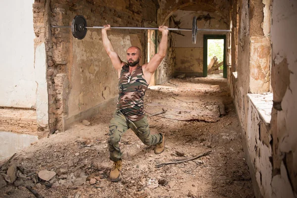 Hombre en ruinas ejercitando el hombro con la barra — Foto de Stock