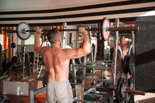 Kaslı adam ağır egzersiz halter salonunda ile omuz için yapmak
