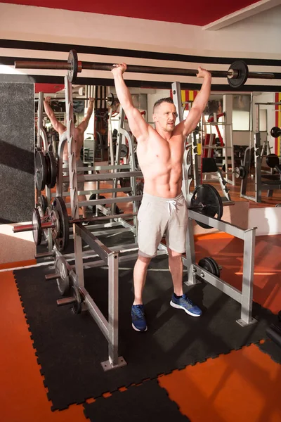 Kaslı adam ağır egzersiz halter salonunda ile omuz için yapmak