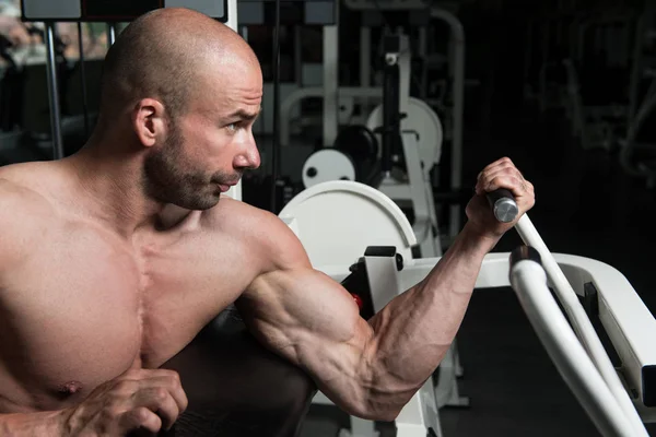 Hombre ejercitando bíceps en la máquina en el gimnasio — Foto de Stock