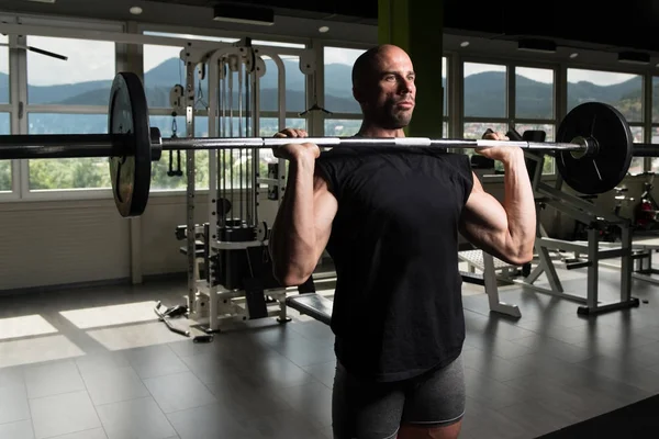 Atleta en el gimnasio ejercitando el hombro con la barra — Foto de Stock