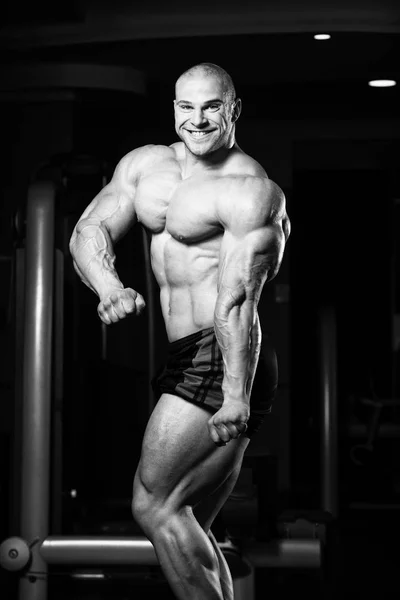 Pohledný svalnatý muž protahuje svaly v tělocvičně — Stock fotografie