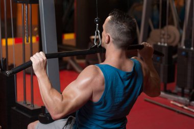 Arka üstünde makine içinde jimnastik salonu için ağır egzersiz yaparak yakışıklı sporcu