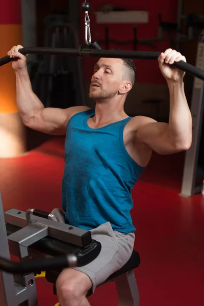 英俊的运动员做在健身房中机上背沉重的杠铃锻炼 — 图库照片