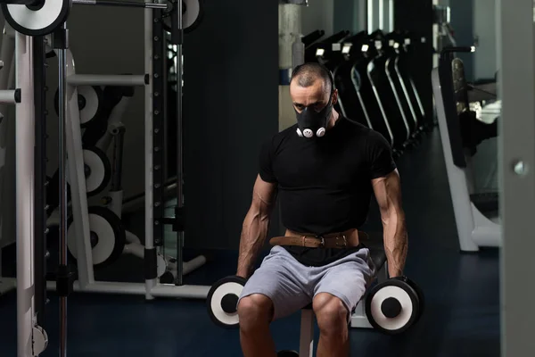 Homem com halteres exercendo bíceps em máscara de elevação — Fotografia de Stock