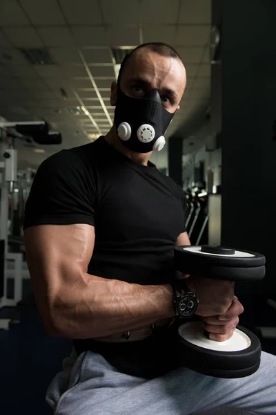 Bodybuilder trainiert Bizeps mit Kurzhanteln in Höhenmaske — Stockfoto
