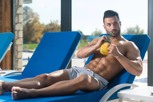 Hombre bebiendo jugo de naranja descansando en los reposeros del sol — Foto de Stock