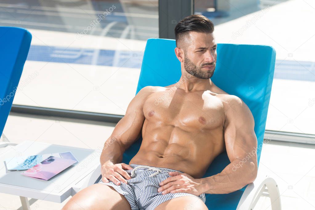 Man Resting On Sun Loungers By Swimming Pool