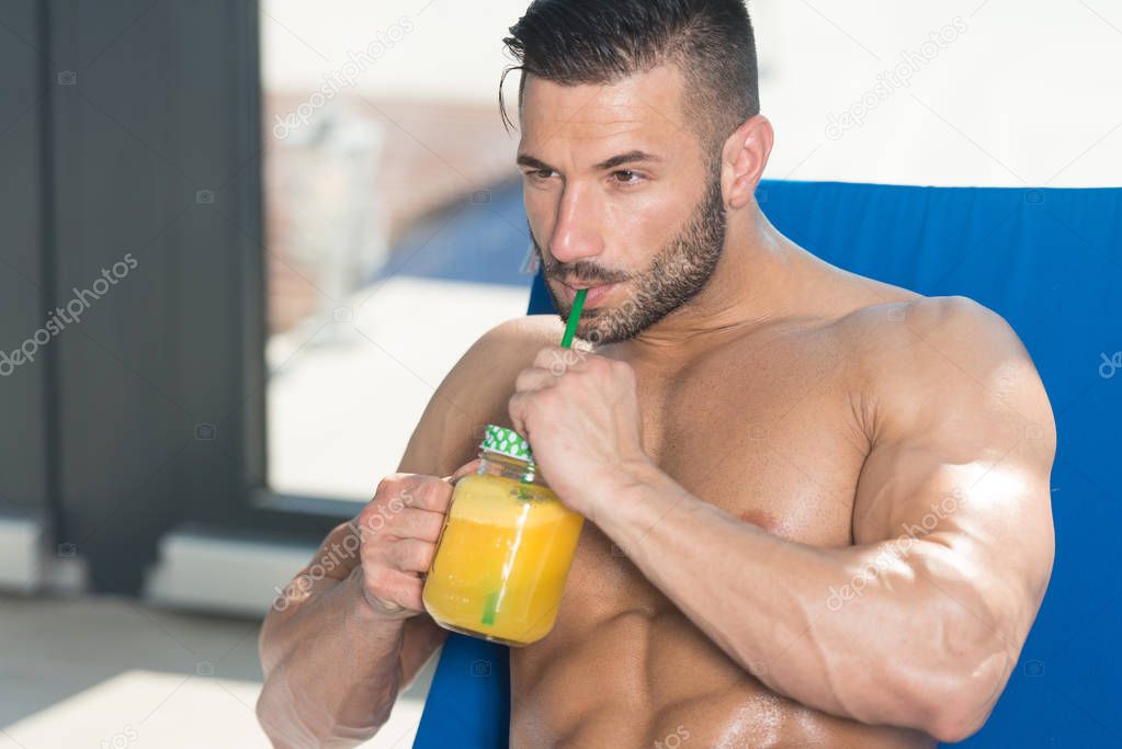 Man Drinking Orange Juice Resting On Sun Loungers