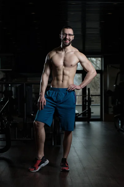 Bodybuilder sérieux portant des lunettes debout dans la salle de gym — Photo