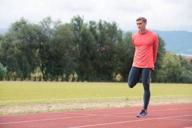 Genç fitness koşucusu koşmadan önce bacaklarını esnetiyor.