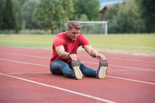Homem de fitness alongamento antes do treino rodando na pista — Fotografia de Stock