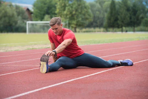 Jovem fitness homem corredor esticando pernas antes de correr — Fotografia de Stock