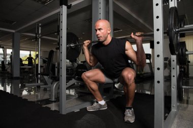 Fitness spor salonu içinde bacaklar egzersiz halter kullanan adam