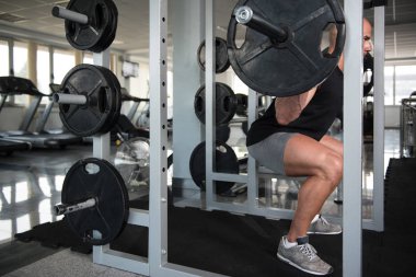 Fitness spor salonu içinde bacaklar egzersiz halter kullanan adam