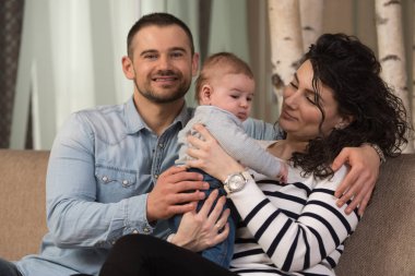 Anne ve baba evdeki kanepede sevimli bebekleriyle oynuyorlar.
