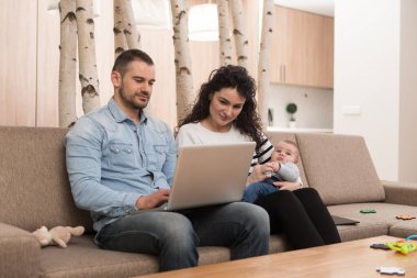 Sevimli Küçük Bebekli Rahat Genç Çift Koltukta Oturuyor, Bilgisayar Oynuyor ve Kullanıyor