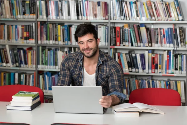 Ευτυχισμένος άνδρας των φοιτητών με το Laptop στη βιβλιοθήκη — Φωτογραφία Αρχείου