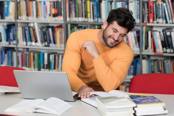 Feliz estudiante masculino con ordenador portátil en la biblioteca —  Fotos de Stock