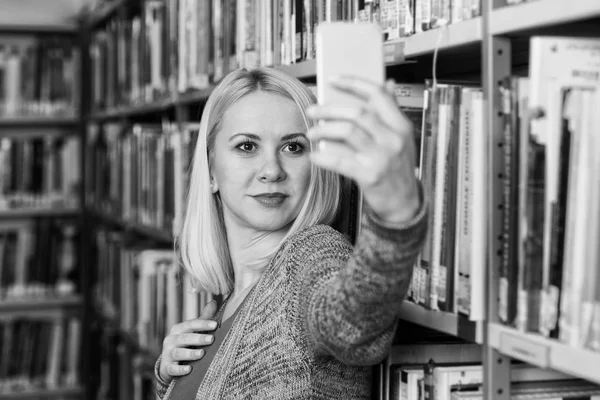 Estudante usando telefone celular para selfie na biblioteca — Fotografia de Stock