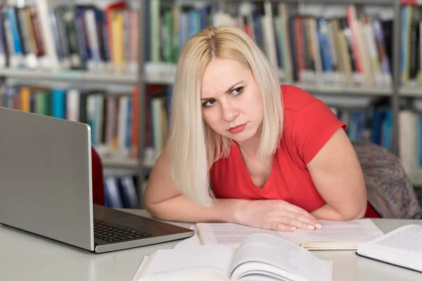 Estudiante cansado trabajando con el ordenador portátil en la biblioteca —  Fotos de Stock