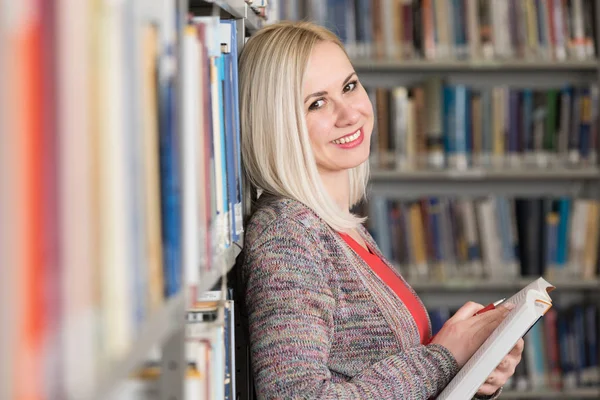 Estudiante feliz leyendo del libro en la biblioteca —  Fotos de Stock