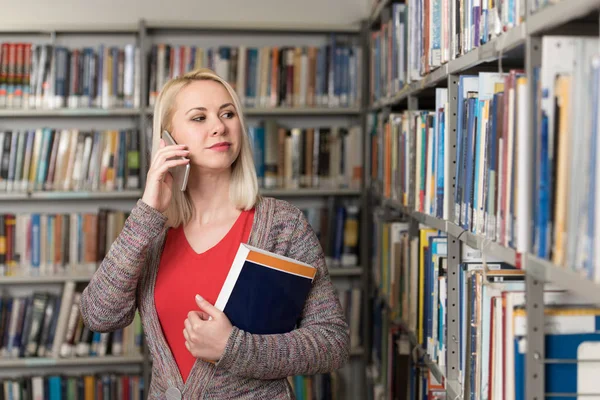 Jolie étudiante utilisant un téléphone portable dans la bibliothèque — Photo