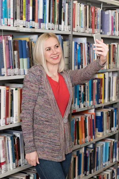 Studentin benutzt Handy für Selfie in Bibliothek — Stockfoto