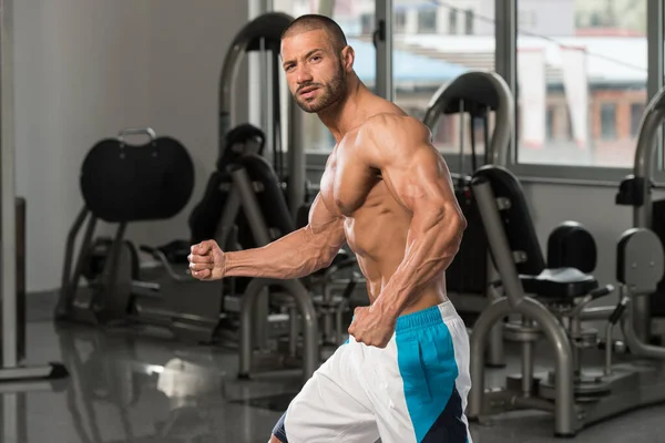 Bizeps-Pose eines jungen Mannes im Fitnessstudio — Stockfoto