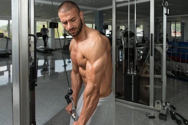 Bodybuilder faisant l'exercice lourd pour des triceps avec le câble — Photo