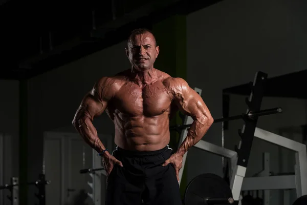 Зрелый мускулистый человек демонстрирует мышцы в спортзале — стоковое фото