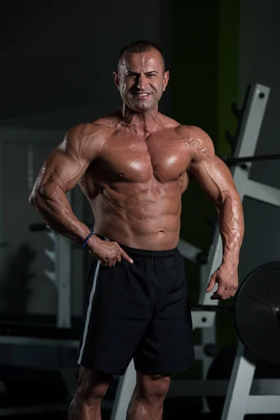 Мускулистый пожилой человек демонстрирует мышцы в спортзале — стоковое фото