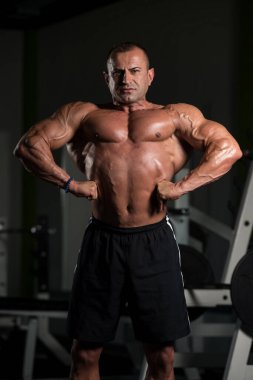 Spor salonunda kaslı, olgun bir adam kaslarını kasıyor.