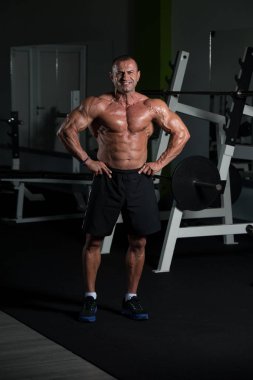 Spor salonunda kaslı, olgun bir adam kaslarını kasıyor.