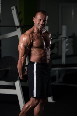Olgun kaslı adam spor salonunda kaslarını esnetiyor.
