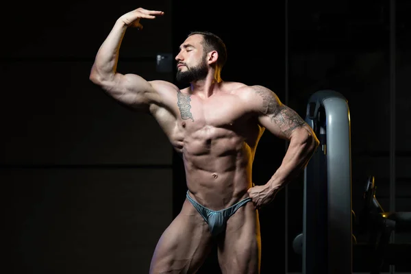 Pose de bíceps de un hombre joven en el gimnasio — Foto de Stock