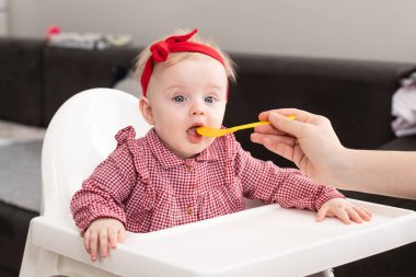 Mutlu anne dadı ya da kız kardeş evde bir kaşık dolusu yiyecekle bir bebeği besler.