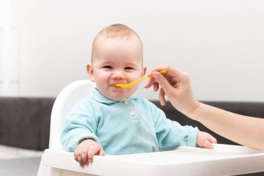 Mutlu anne dadı ya da kız kardeş evde bir kaşık dolusu yiyecekle bir bebeği besler.