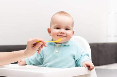 Anne, bebeğini kaşıkla besliyor. Anne, sevimli çocuğuna sağlıklı yiyecekler veriyor.