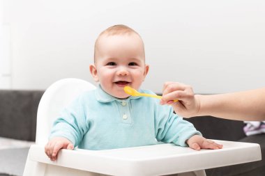 Anne, bebeğini kaşıkla besliyor. Anne, sevimli çocuğuna sağlıklı yiyecekler veriyor.