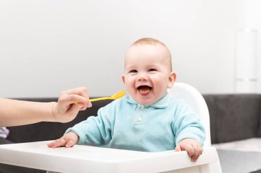 Mutlu anne dadı ya da kız kardeş evde bir kaşık dolusu yiyecekle bir bebeği besler.