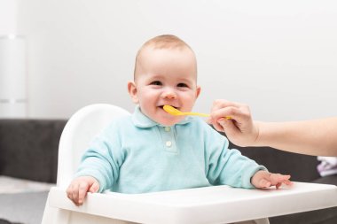 Anne, bebeğini kaşıkla besliyor. Anne, sevimli çocuğuna sağlıklı yiyecekler veriyor.