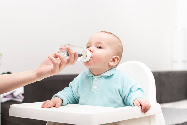 Mother Giving Her Baby Child Son Water To Drink From Bottle At Home