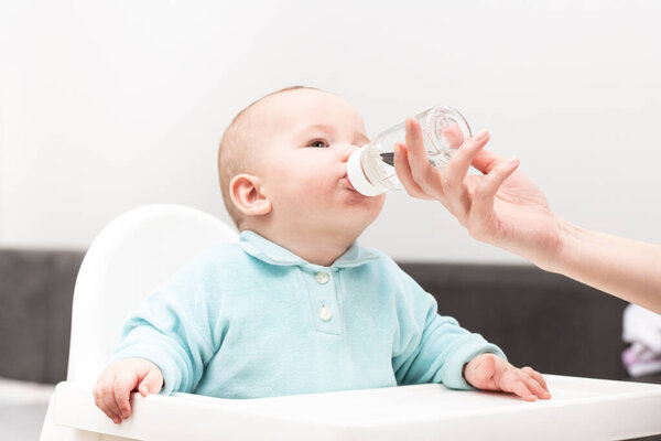 Mother Giving Her Baby Child Son Water To Drink From Bottle At Home