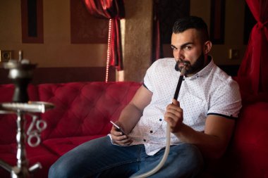 Genç Adam Shisha 'yı Arap restoranında tüttürüyor - Adam nargile soluyor ve telefonda mesajlaşıyor