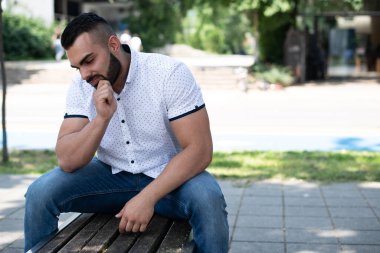 Park 'ın dışında bankta oturan, kendinden emin ve başarılı, beyaz gömlekli genç bir adamın portresi.