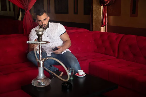 男は背景にカラフルな壁とカフェでトルコのフカを喫煙し 電話でテキストメッセージ — ストック写真