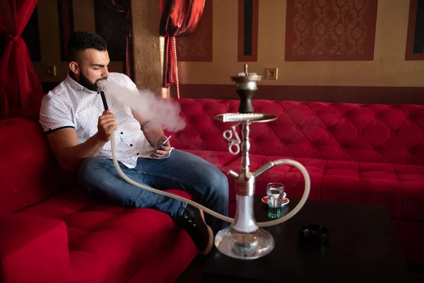 男子吸烟土耳其胡卡在咖啡馆与五颜六色的墙背景和短信电话 — 图库照片