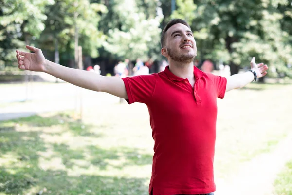 腕を伸ばして屋外に立つ赤いTシャツの陽気な若い男の肖像画 — ストック写真